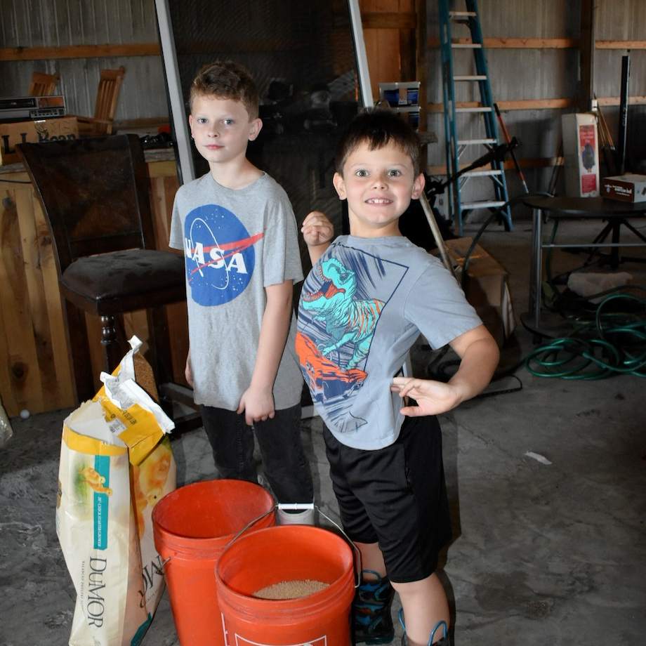 Two young kids standing next to some feed buckets